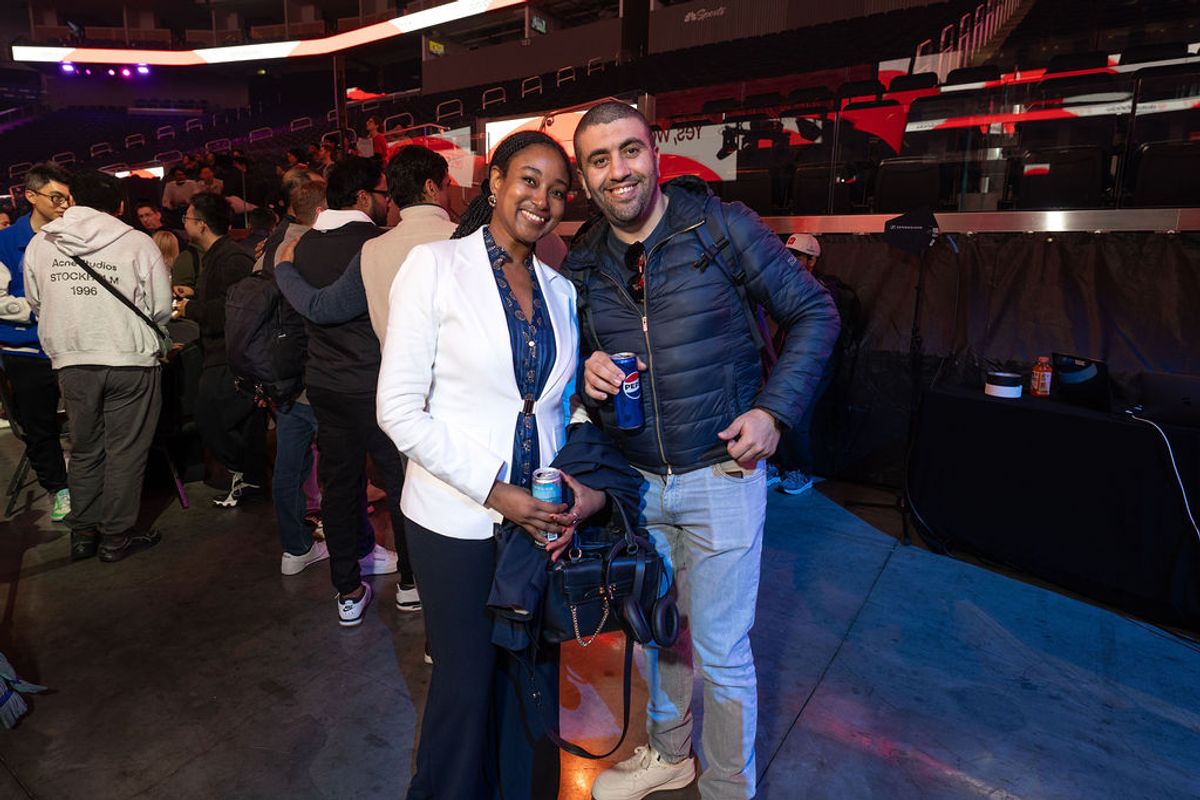 Two attendees pose together at a conference event in an arena setting with crowds in the background.