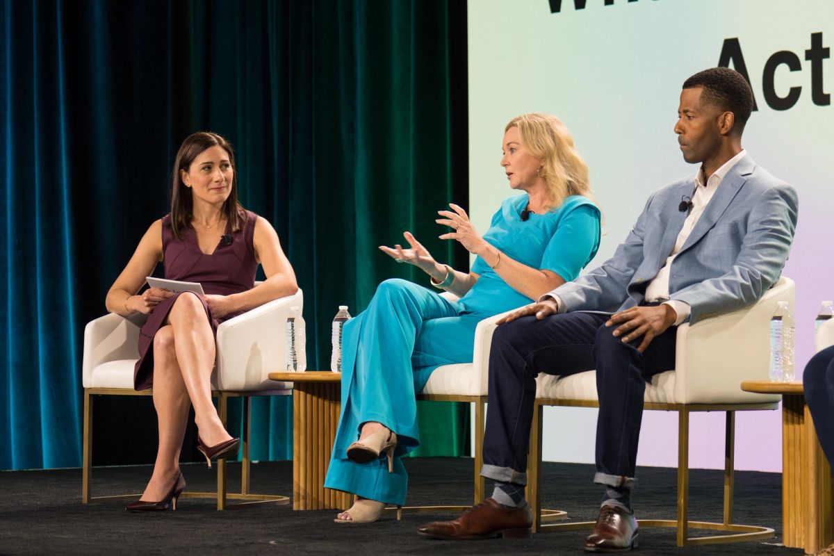 Three panelists seated on stage in discussion at a conference.