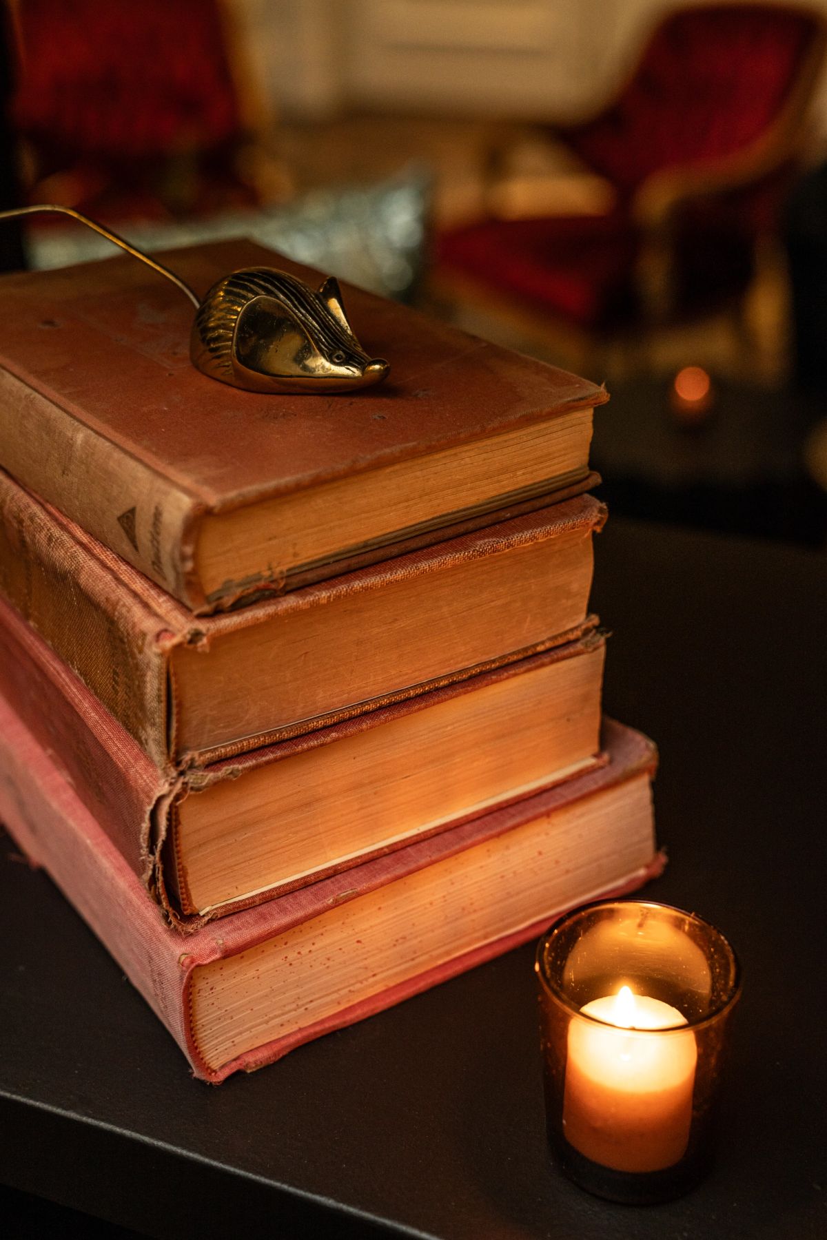 Stack of old leather-bound books with ornate metal clasp on top, lit candle beside them in warm interior