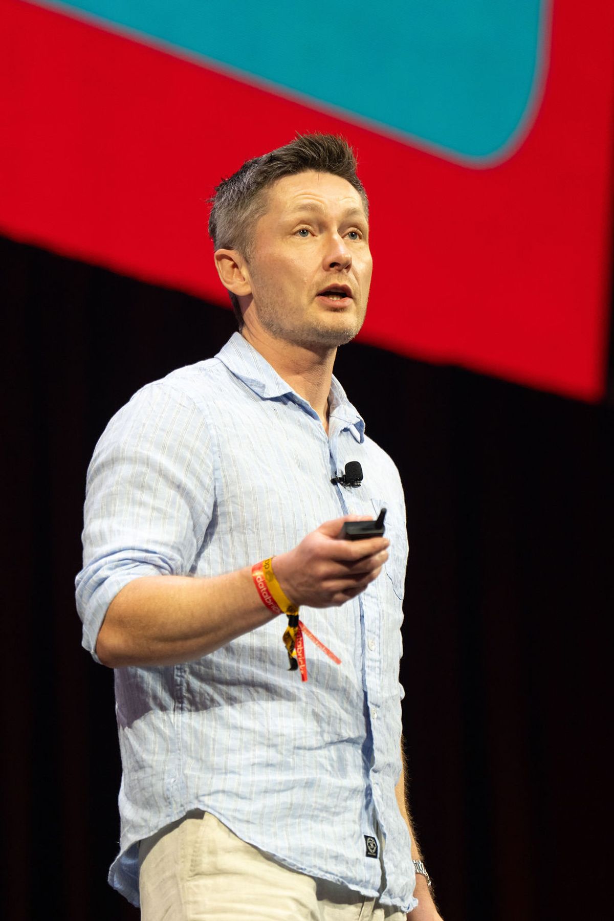 Speaker presenting on stage with microphone and red lighting in background at conference venue
