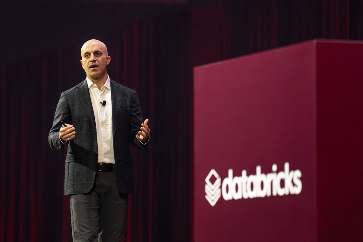 Executive presenting on stage next to large red Databricks sign at conference venue