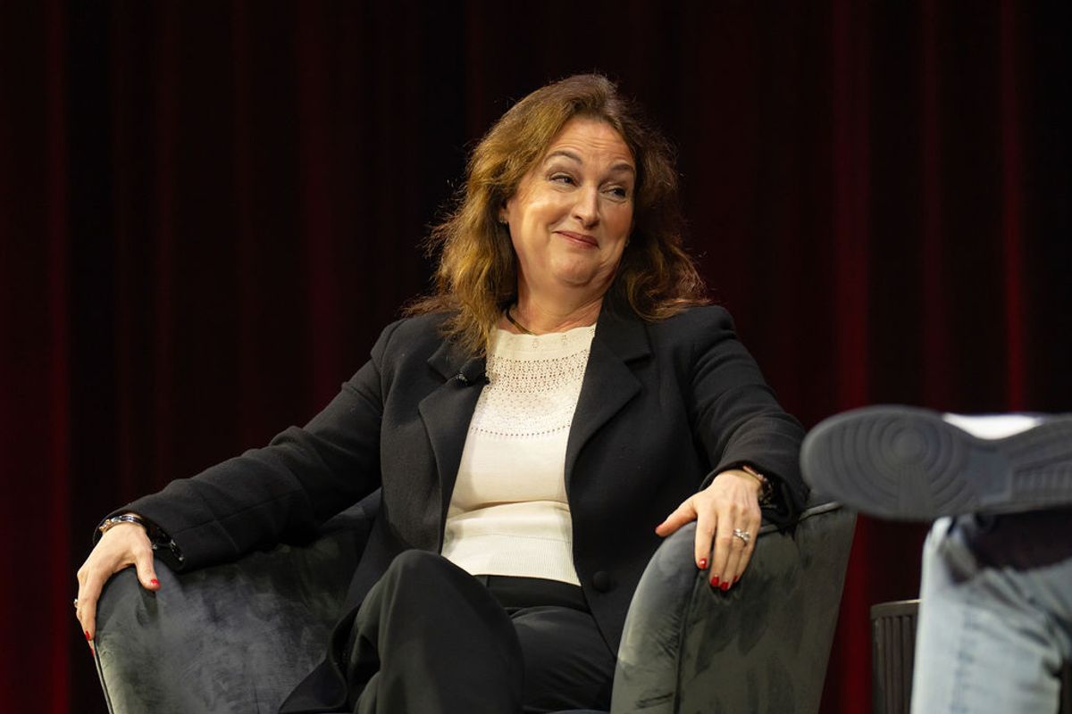 Woman in dark blazer and white top sits in gray armchair during conference panel discussion