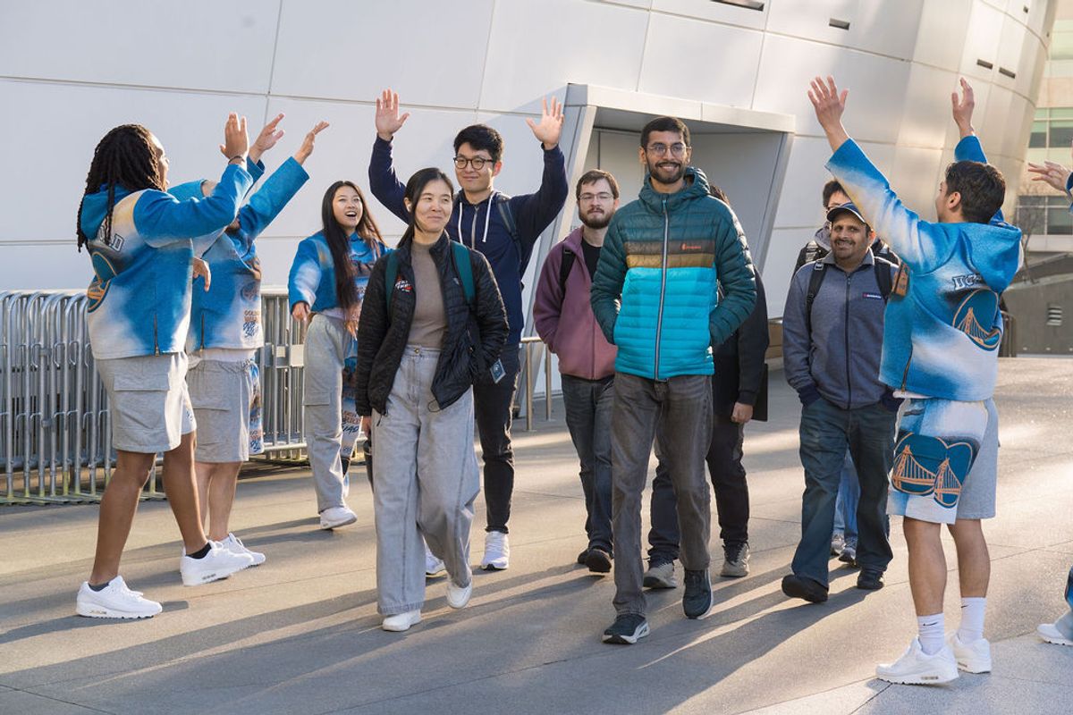 Group of conference attendees celebrating with raised hands outside modern building entrance