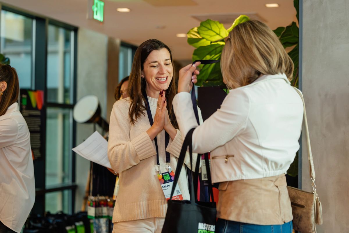 Two women in business attire giving each other a high-five at a networking event in a modern office space.