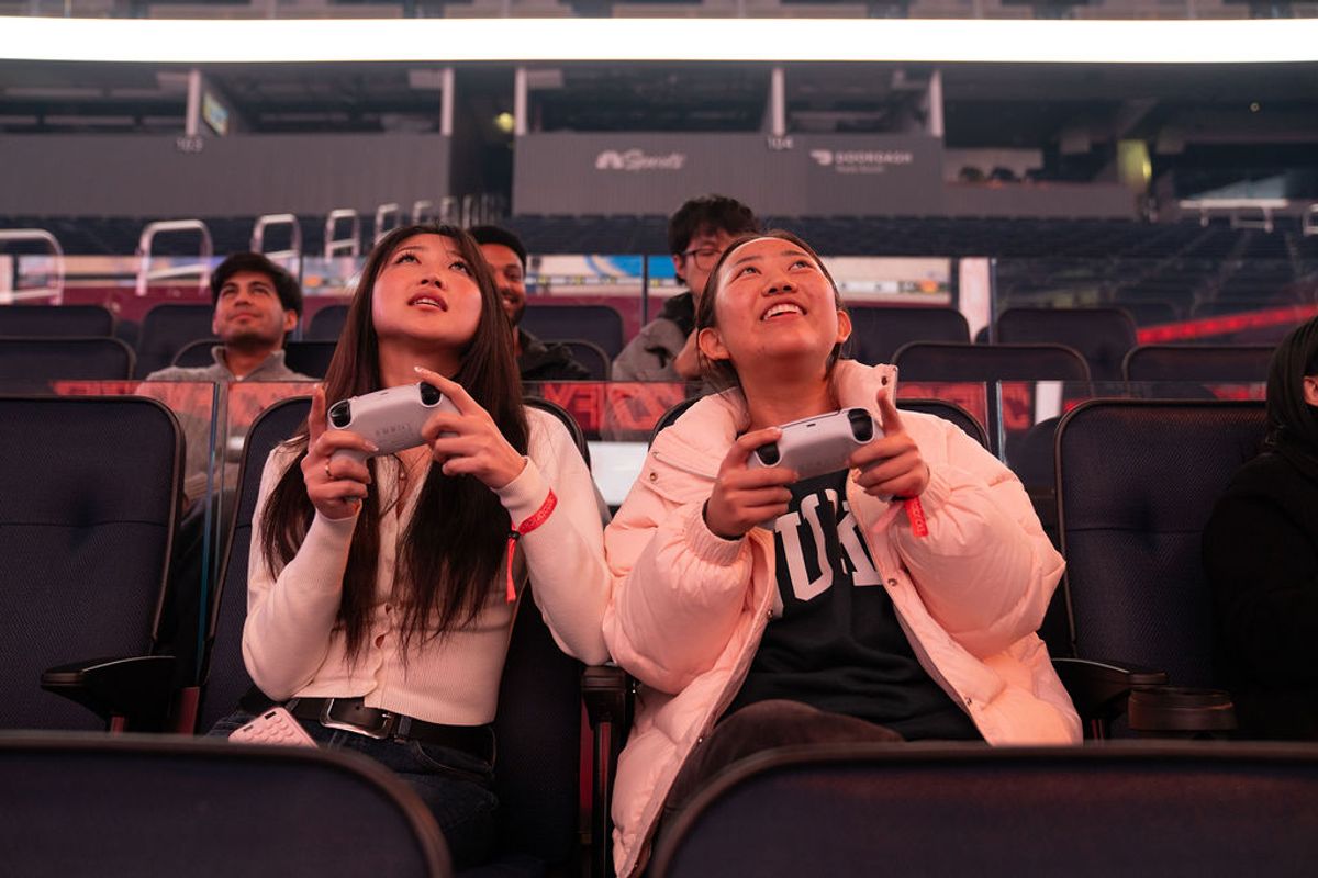 Attendees with game controllers look up at screens during an interactive gaming session at a conference venue.