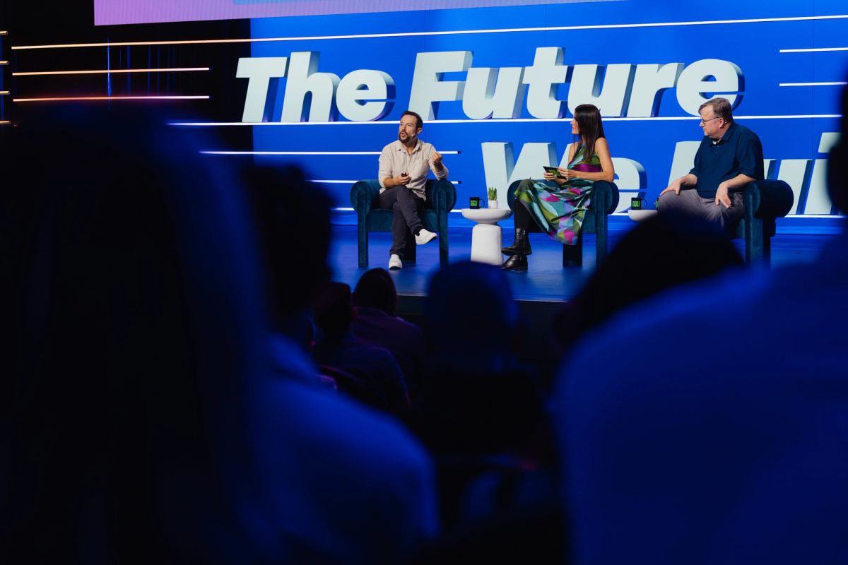 Three panelists seated on white chairs discussing "The Future" on stage with blue backdrop before audience
