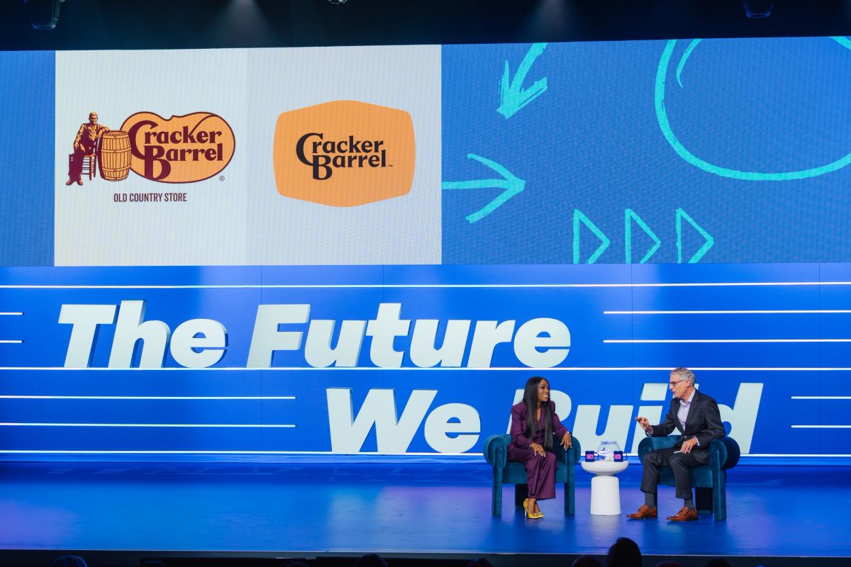 Two speakers sit in blue chairs on stage with "The Future We Build" backdrop and Cracker Barrel logos