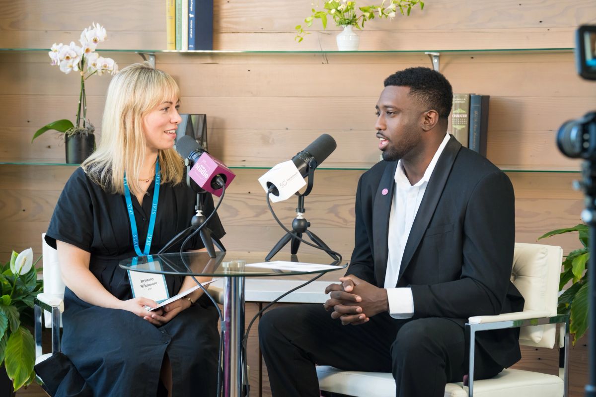 Female interviewer with microphone and male interviewee in suit sitting at table during podcast recording