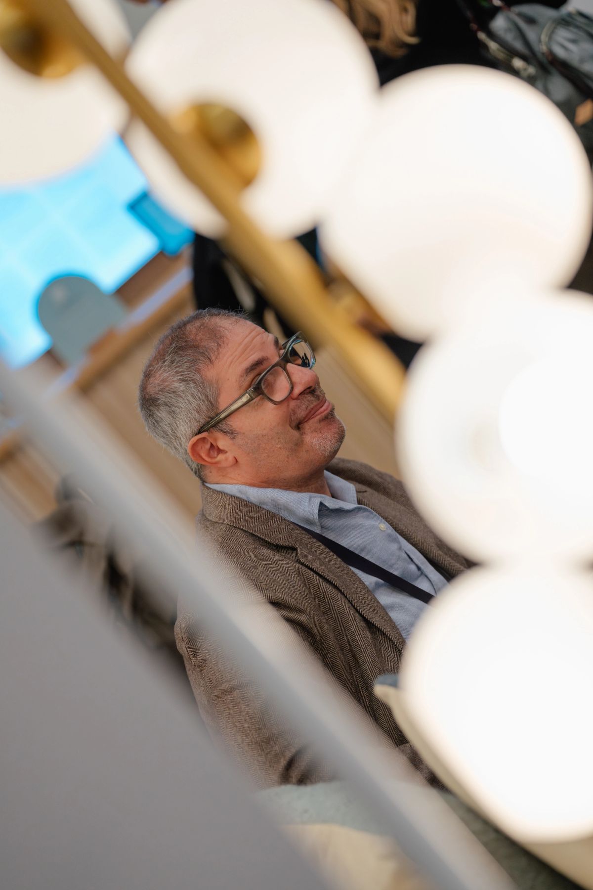 Smiling man with glasses and beard sitting at conference, viewed through blurred white foreground objects