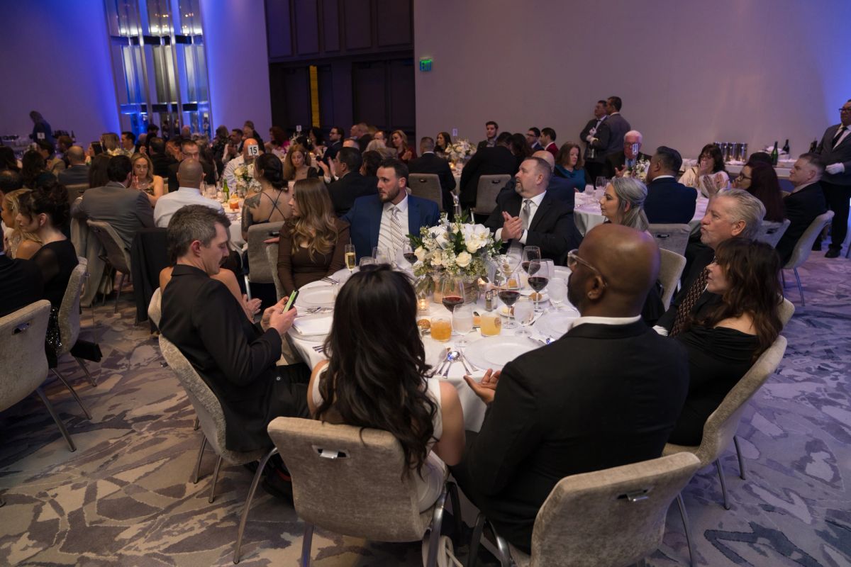 Formal dinner event with guests seated at round tables with white linens and floral centerpieces in elegant.