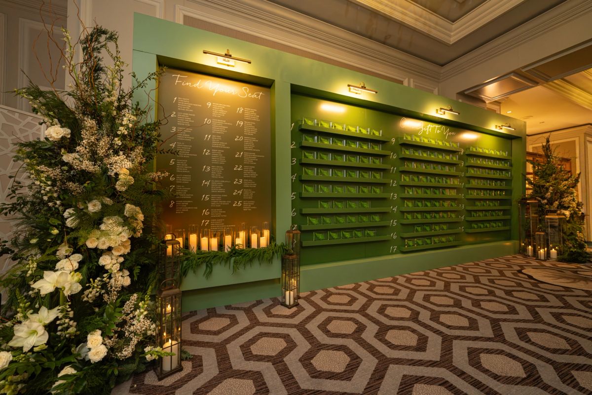 Green escort card display wall with white flowers and geometric patterned carpet in elegant hotel lobby