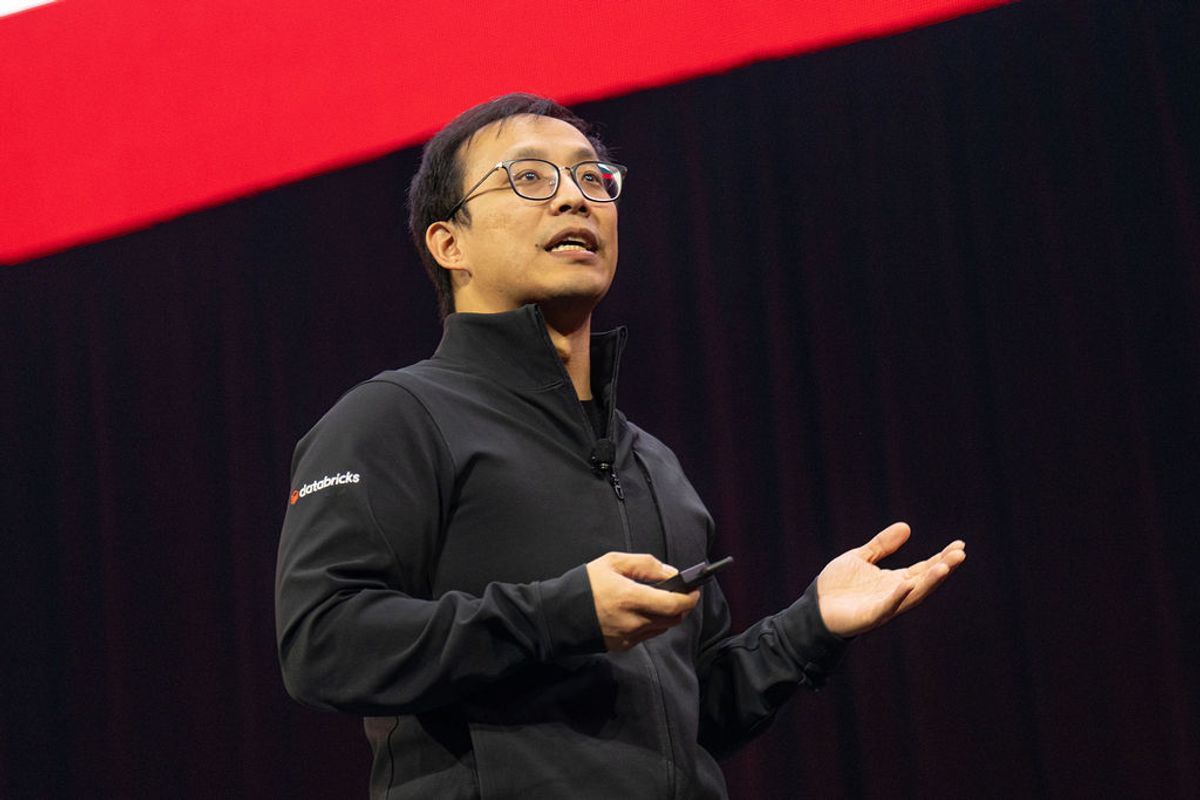 Executive presenting on stage at conference, wearing black jacket and glasses, gesturing while speaking