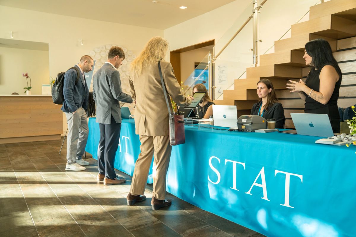 Conference attendees register at blue STAT branded reception desk with laptops in modern lobby