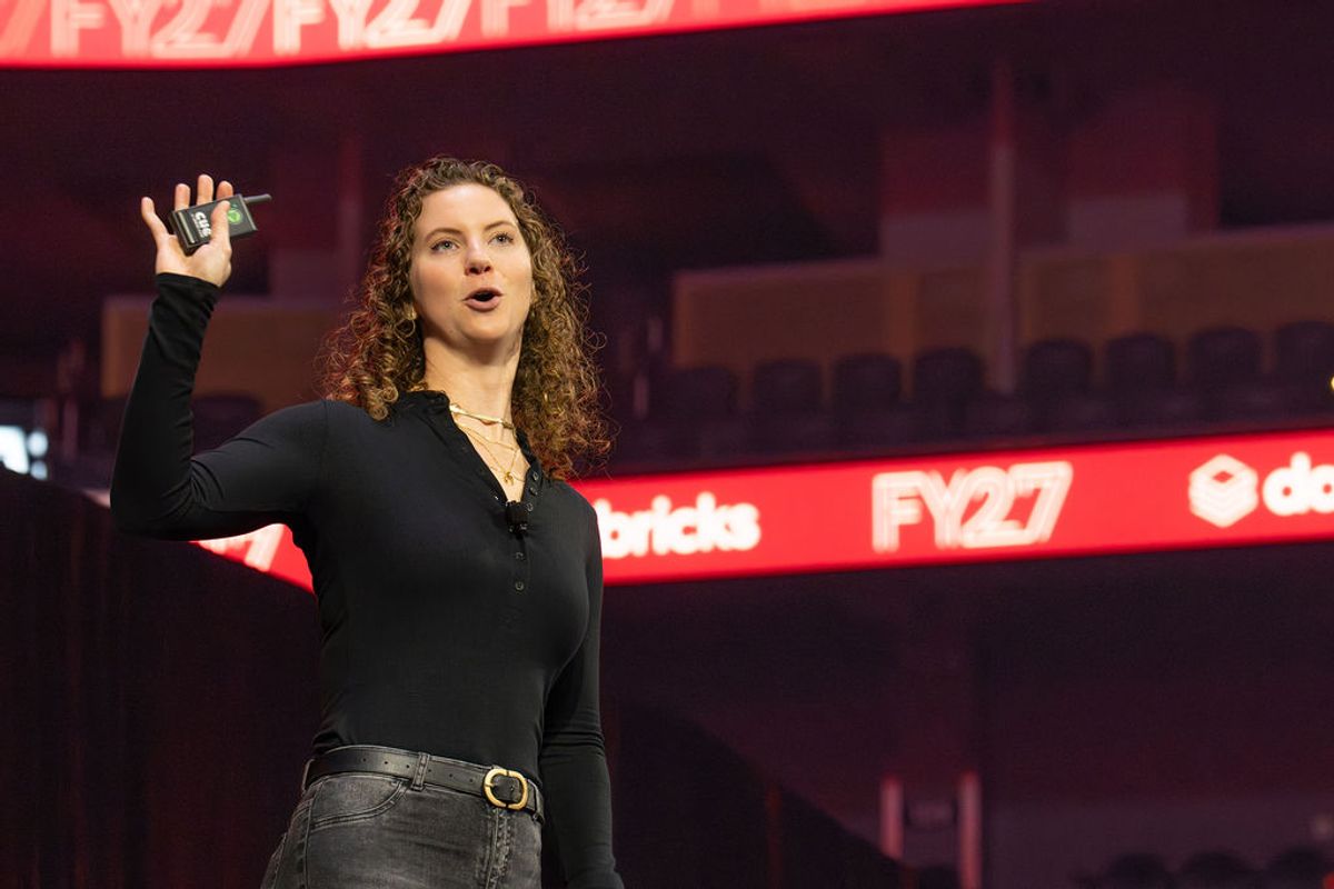 Speaker presenting on stage with curly hair gesturing while speaking at technology conference
