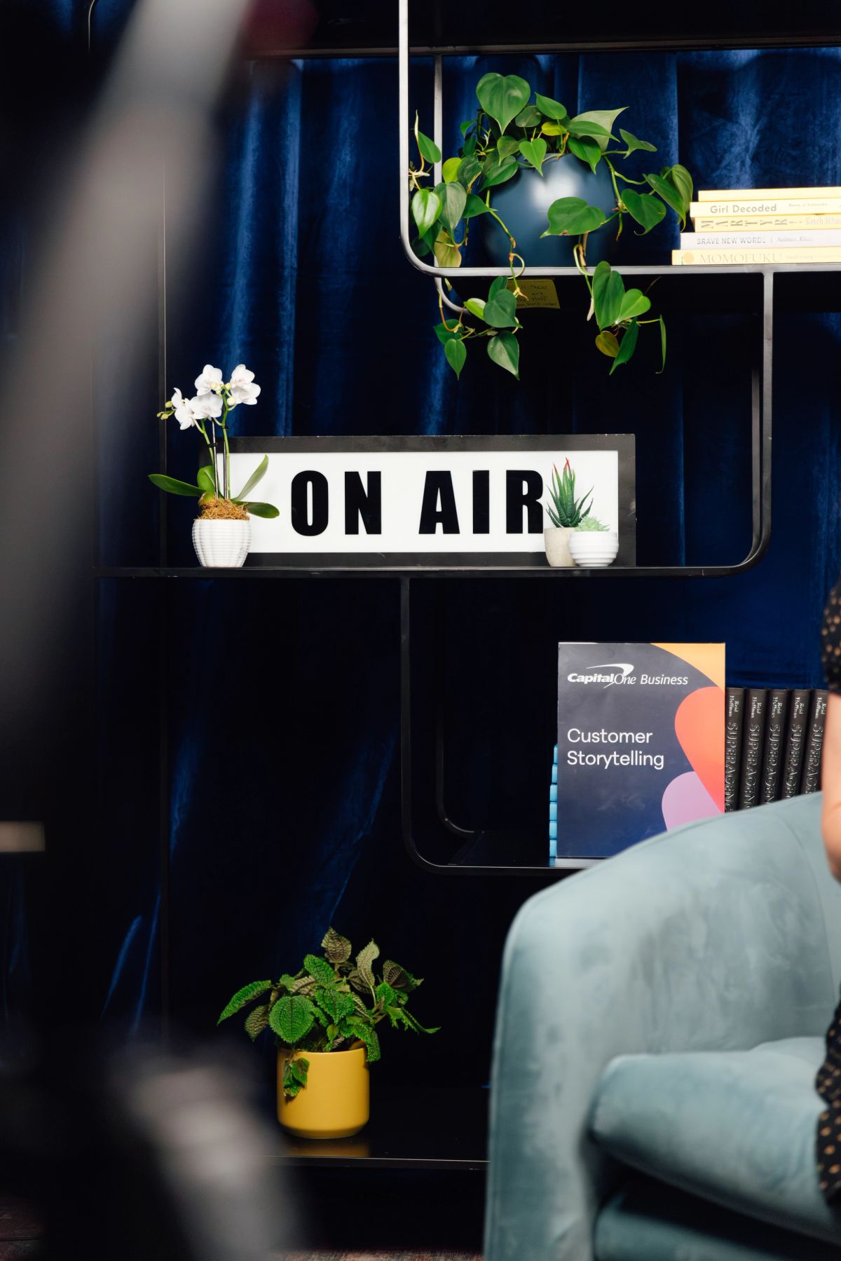 Modern office shelf with "ON AIR" lightbox sign, potted plants, and business books against blue wall