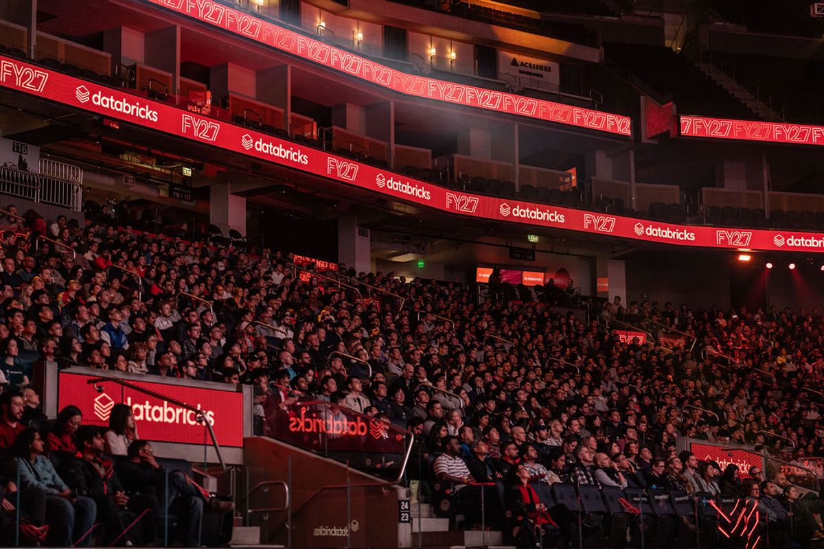 Large audience seated in tiered arena seating with red Databricks branding and lighting throughout venue