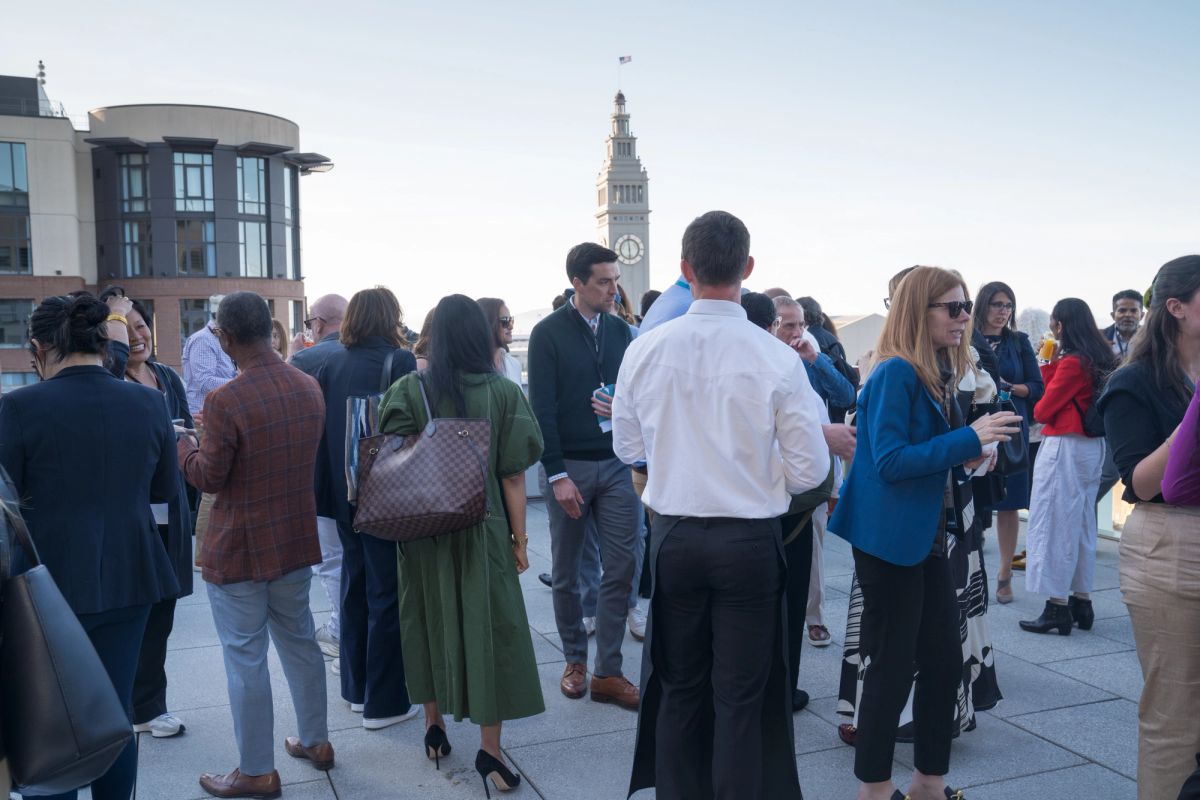 Attendees networking at an outdoor reception with a clock tower and modern building in the background