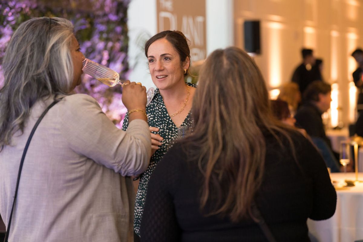 Three women networking and conversing at an indoor reception event with ambient lighting