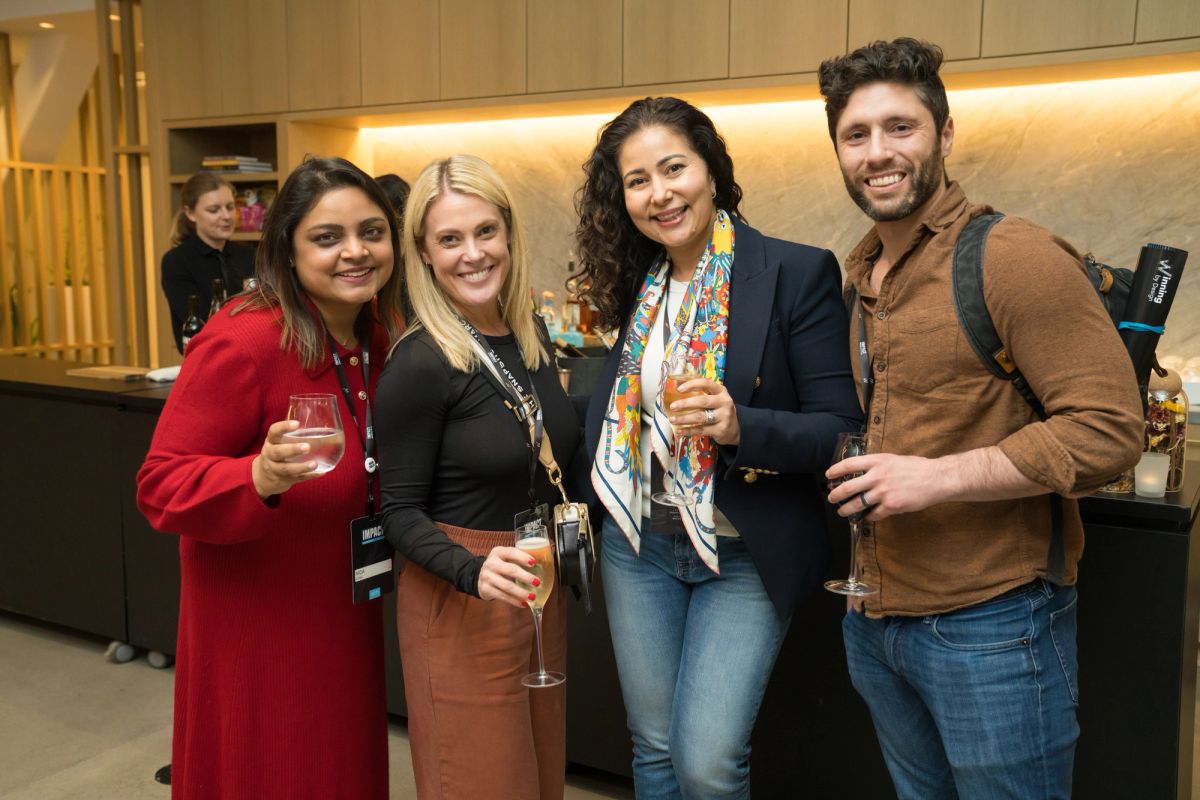Four conference attendees holding drinks and smiling together in a modern venue lobby