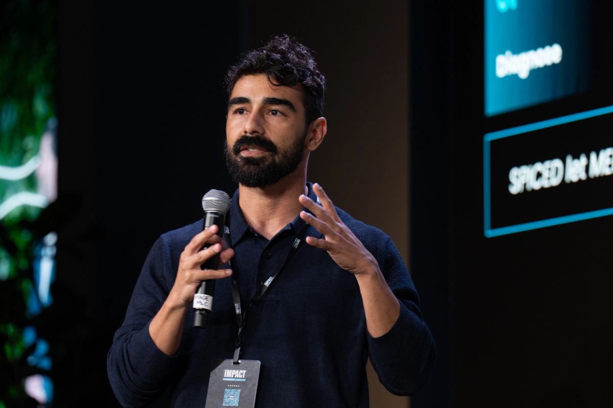 Speaker with microphone presenting at conference, gesturing with hand while speaking on stage