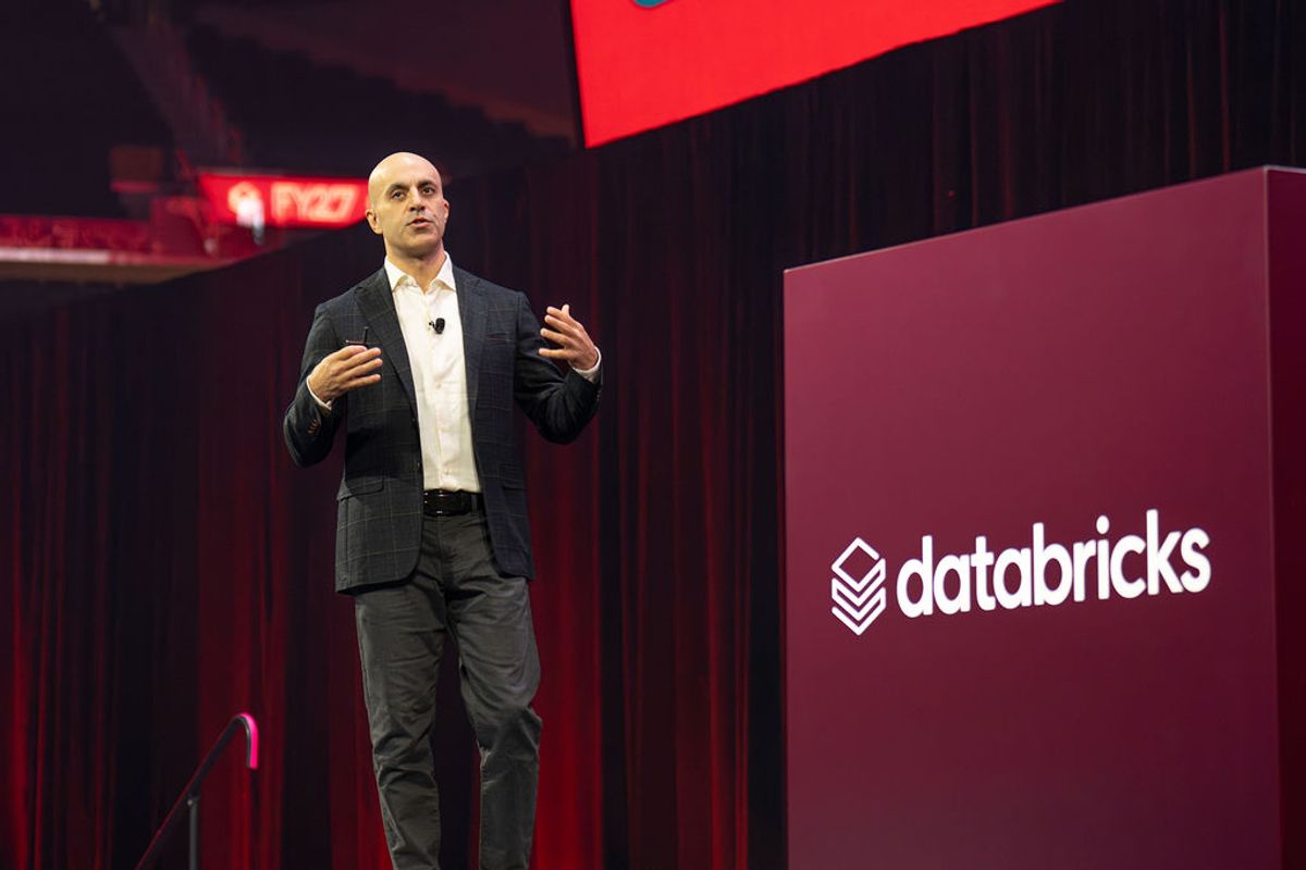 Executive presenting on stage next to large Databricks podium at conference venue with red lighting