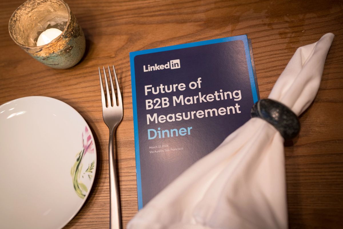 Person's hands holding LinkedIn "Future of B2B Marketing Measurement Dinner" program at table with plate and.