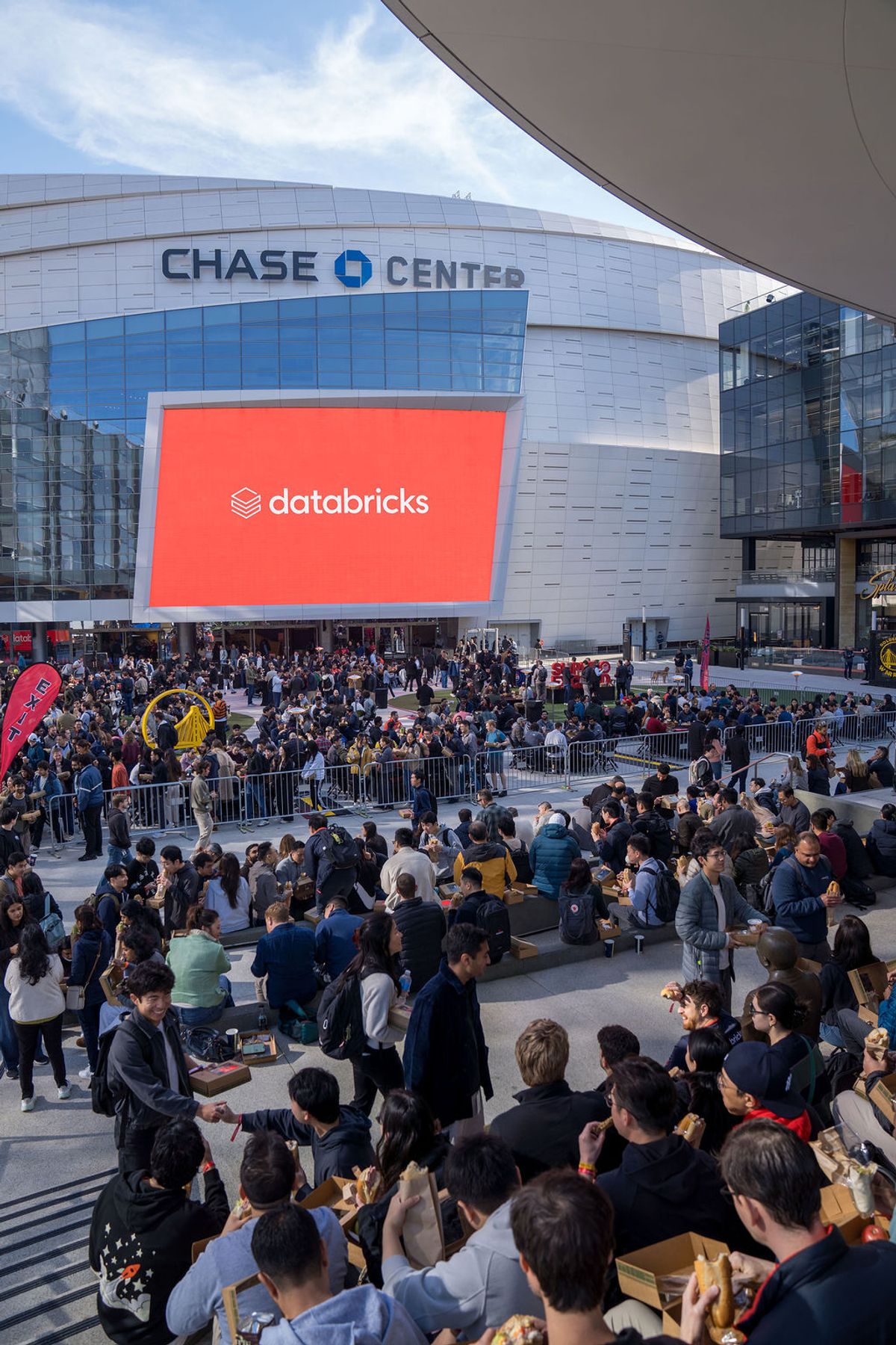 Large crowd of conference attendees gathered outside Chase Center with Databricks logo on building screen