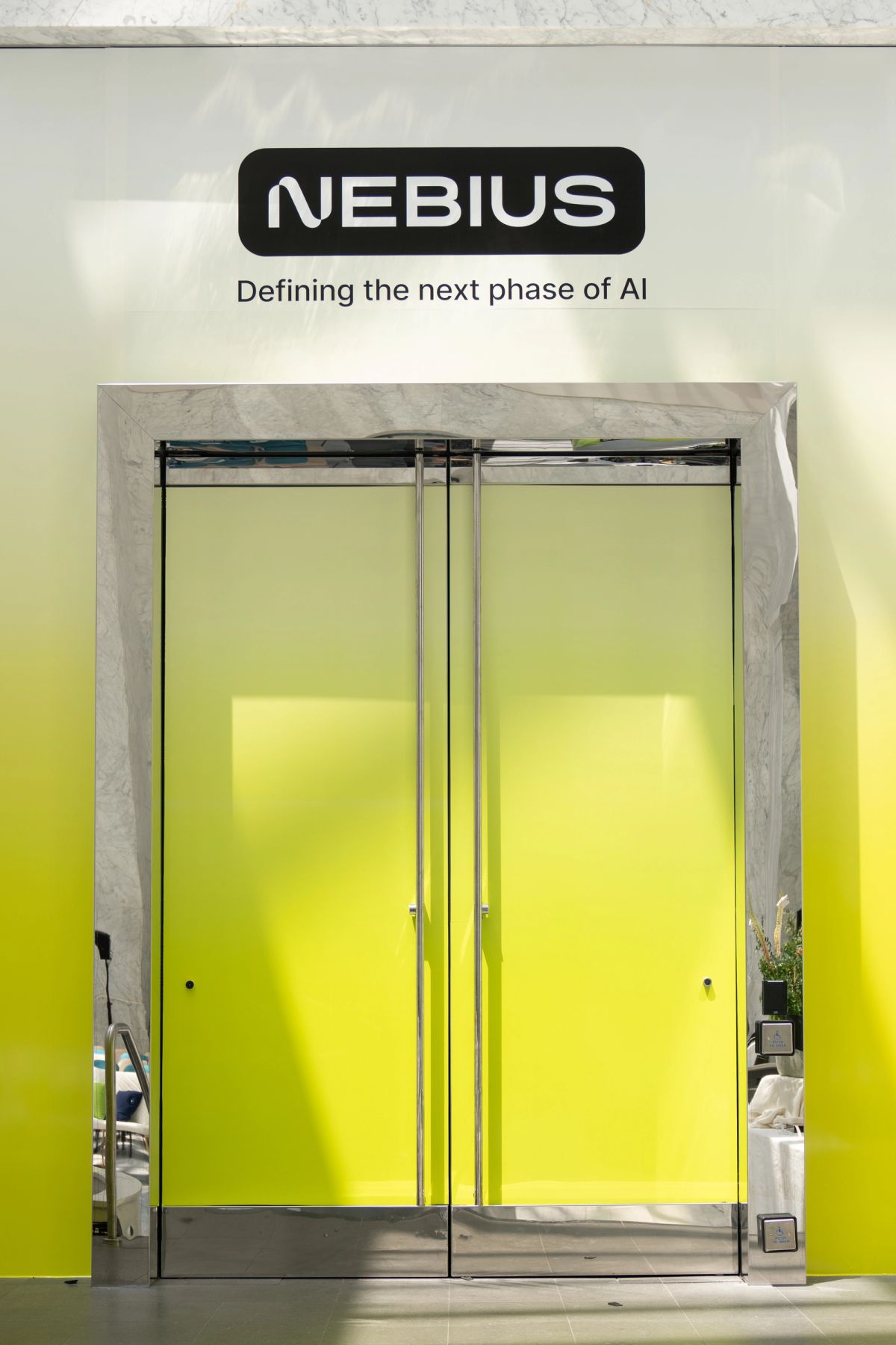 Nebius "Defining the next phase of AI" signage above yellow-green glass doors at a conference.