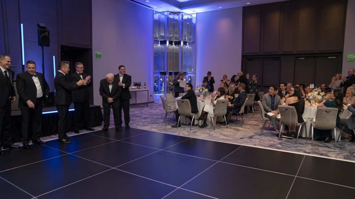 Formal gala event with speakers presenting to seated guests at round tables in elegant venue with blue.