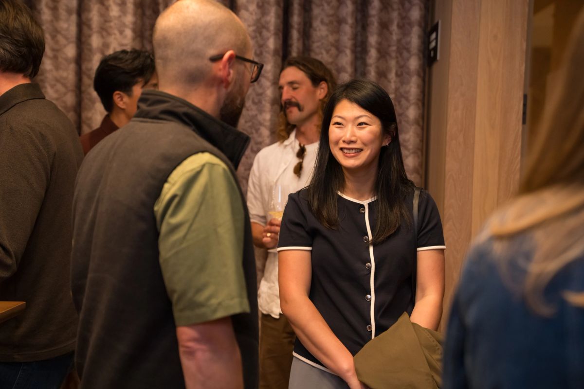 Attendees networking at an indoor event, with a woman in a dark blouse smiling in the foreground