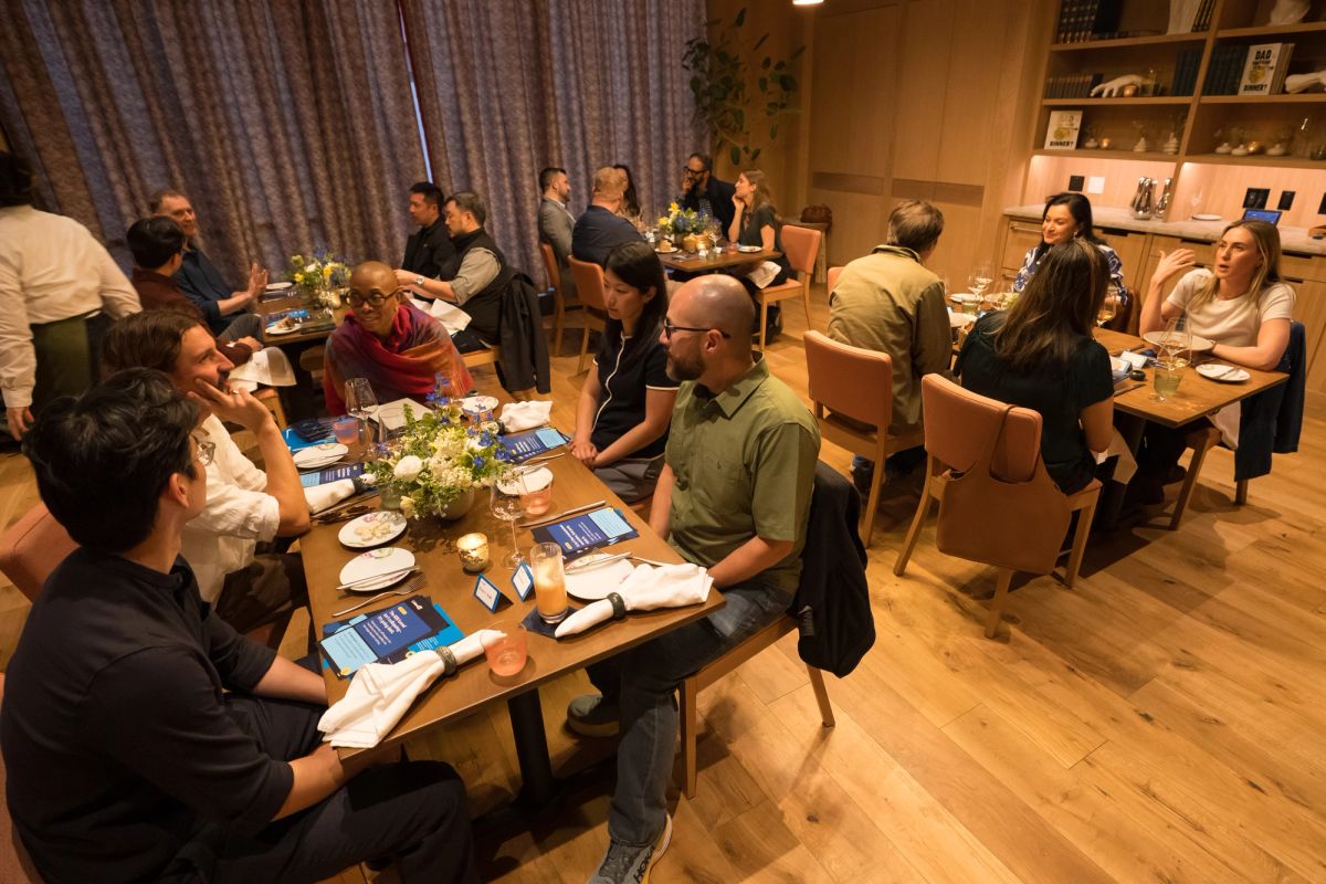 Attendees seated at tables with materials during an indoor panel discussion event