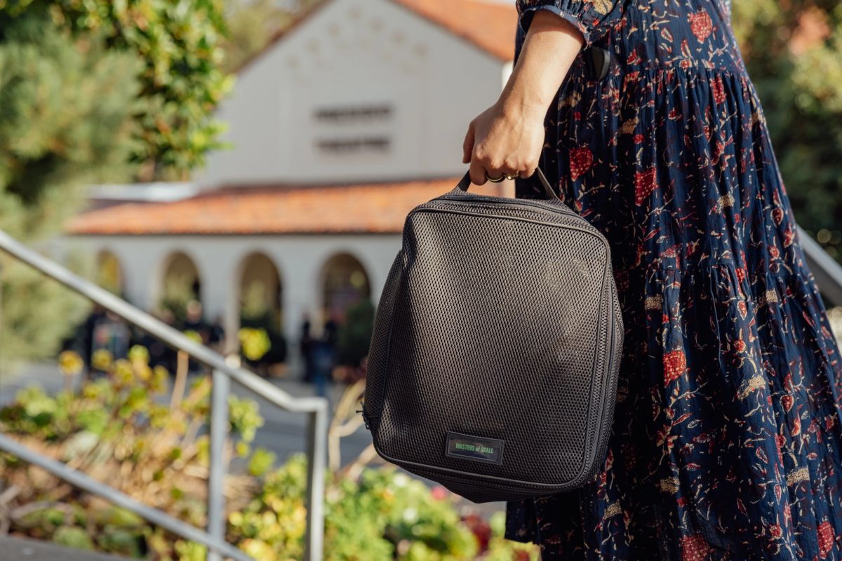 Person in floral dress carrying black bag walks past building with arched windows and greenery