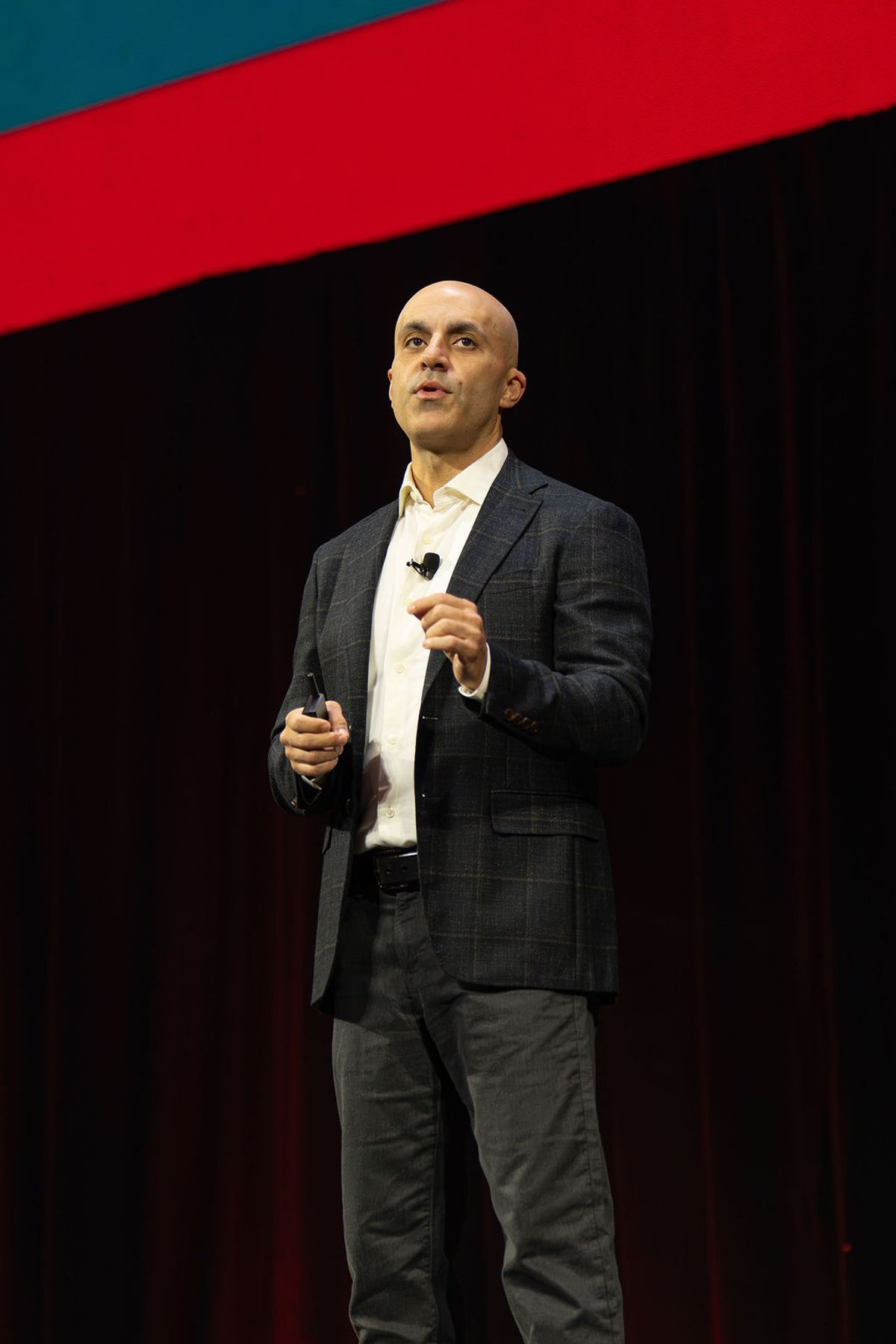 Bald speaker in gray suit and white shirt presenting on stage with microphone at conference venue