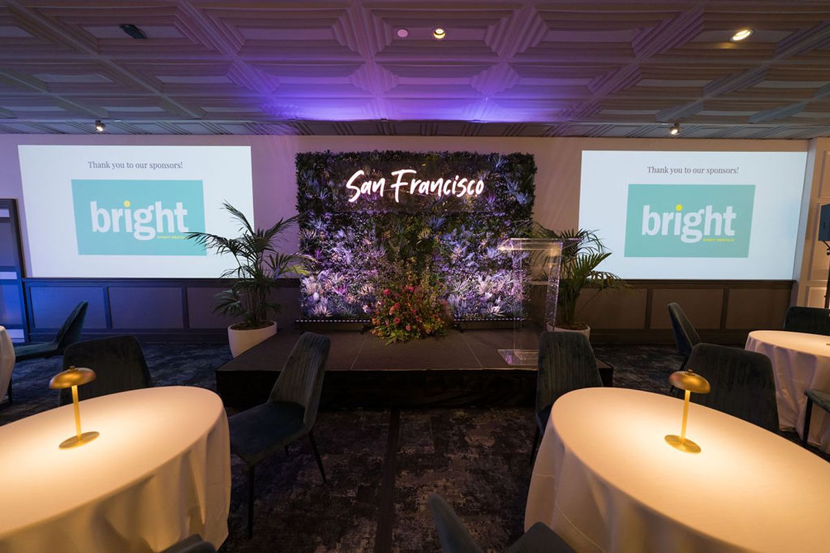 Reception setup with bright branded screens, San Francisco floral backdrop, and cocktail tables with lighting