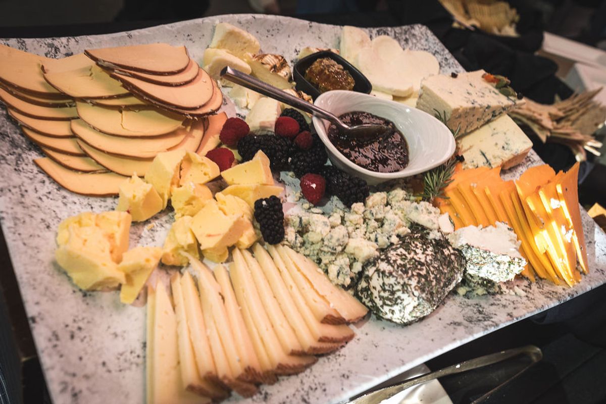 Cheese and charcuterie board with sliced apples, crackers, various cheeses, olives, and jam at conference.