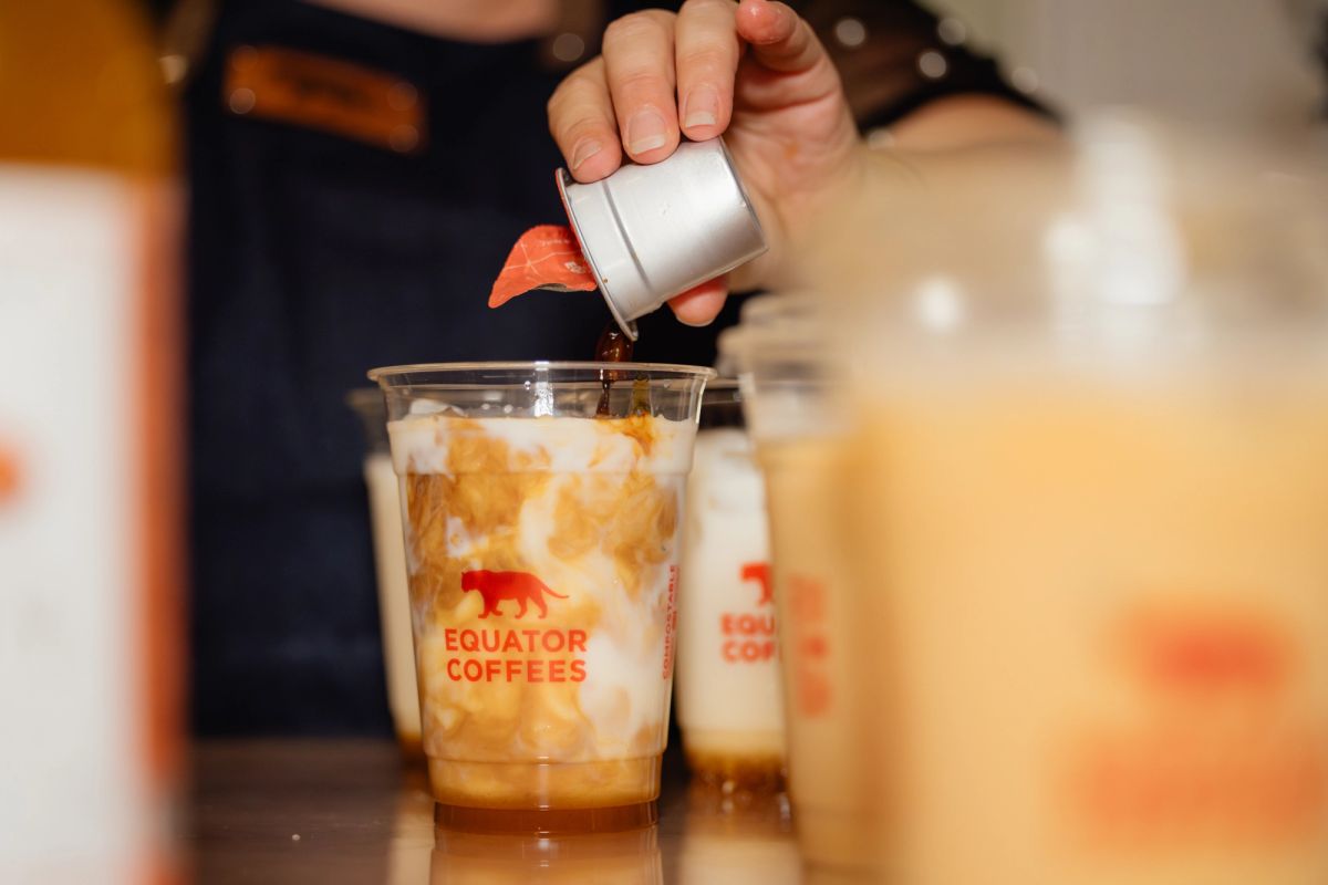 Barista pouring milk into iced coffee drinks at Equator Coffees station during conference event