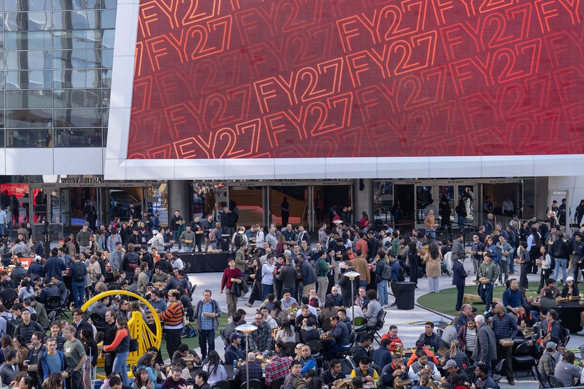 Large crowd of attendees gathered in outdoor plaza area with red FY27 branded building backdrop