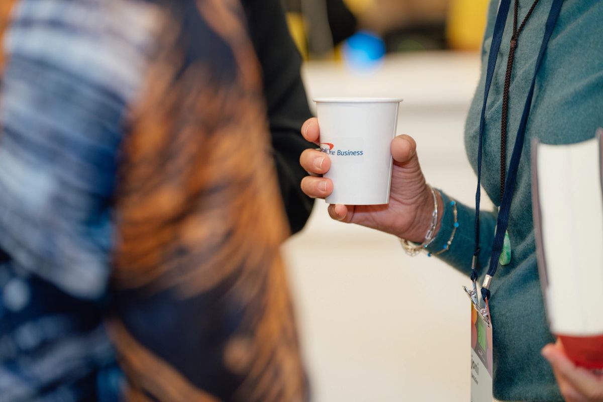 Conference attendee holds white cup with blue text while networking at business event