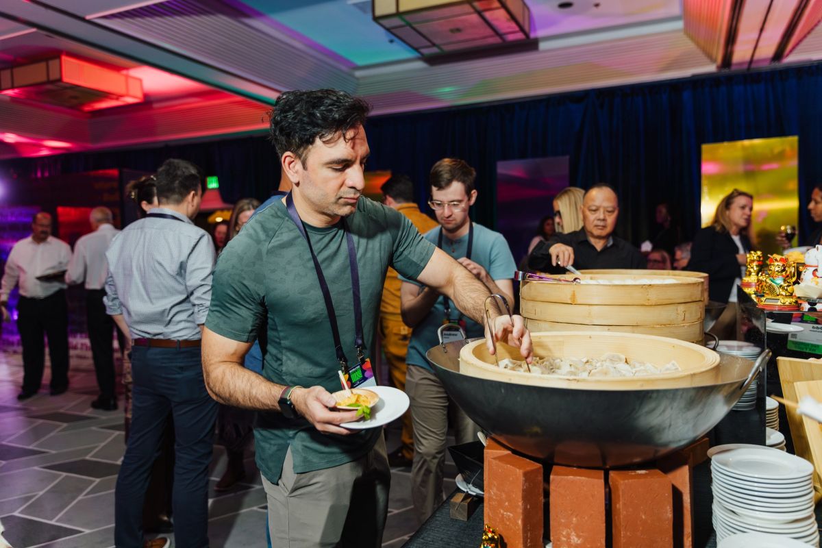 Man in green shirt serving food from large bowl at conference networking event with colorful lighting