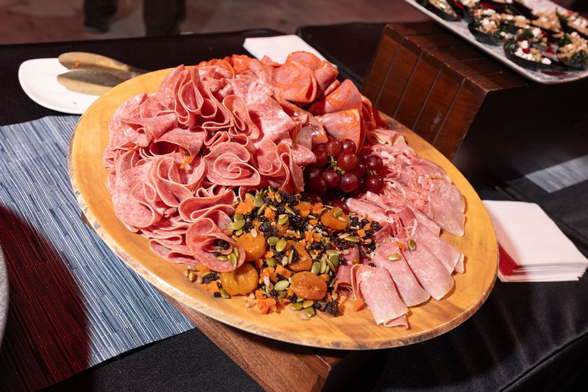 Wooden platter of assorted cured meats and nuts with garnish on conference table setting