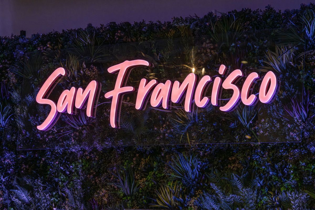 Pink neon "San Francisco" text overlaid on tropical foliage with purple evening sky in background.
