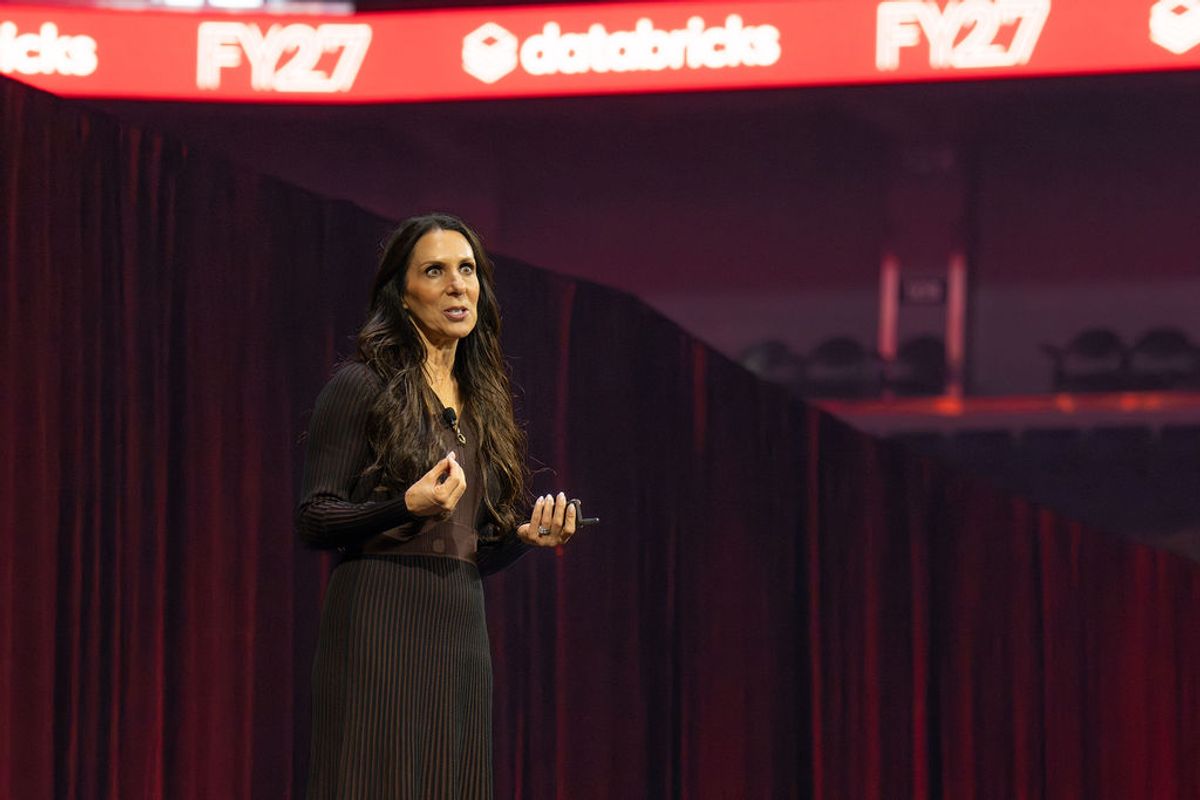 Speaker presenting on stage with red lighting and branded backdrop at conference venue