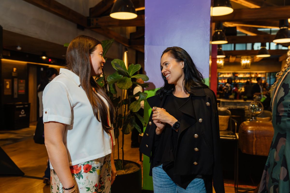 Two women networking and conversing in a modern restaurant or hotel lobby with exposed beams and pendant.