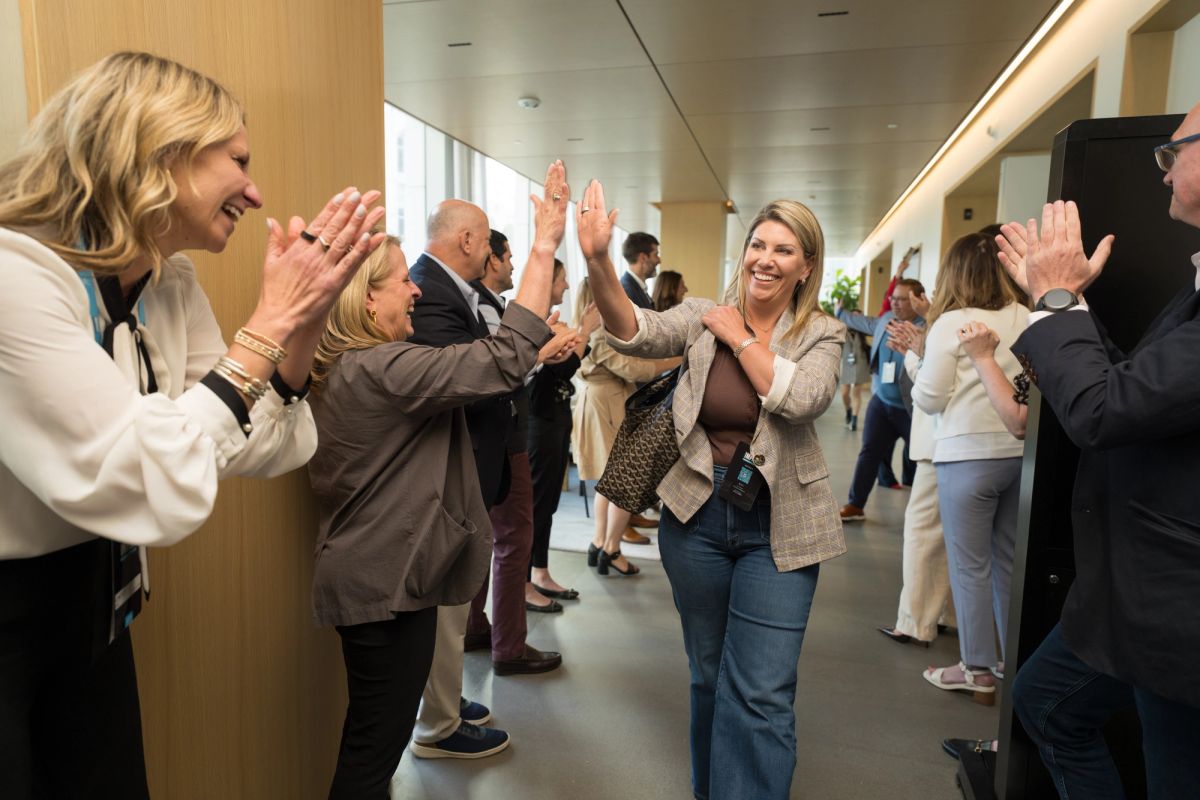 Conference attendees giving high-fives and applauding in a modern building corridor during a networking event.