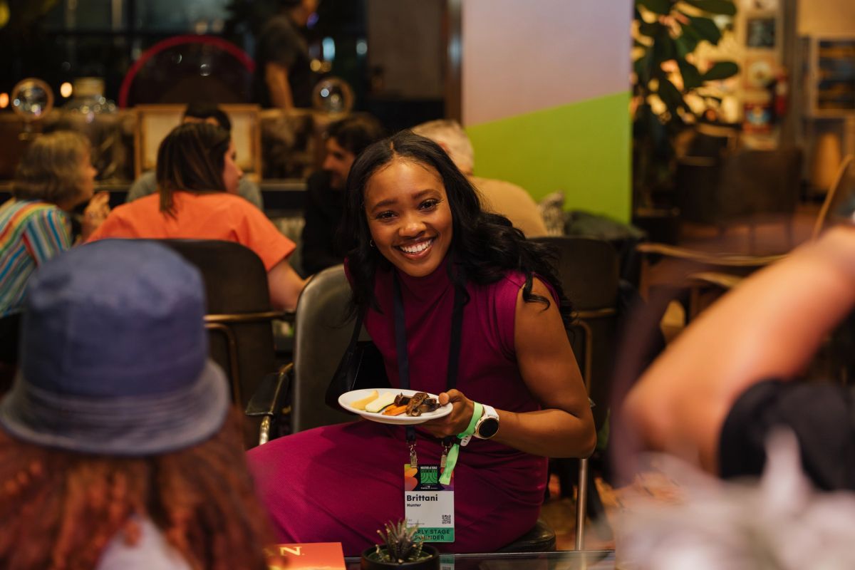 Woman in purple dress smiling while holding a plate of food at a conference networking event