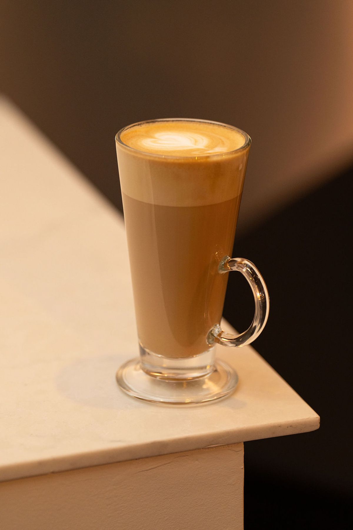 Latte with foam art in glass mug on wooden surface at indoor venue