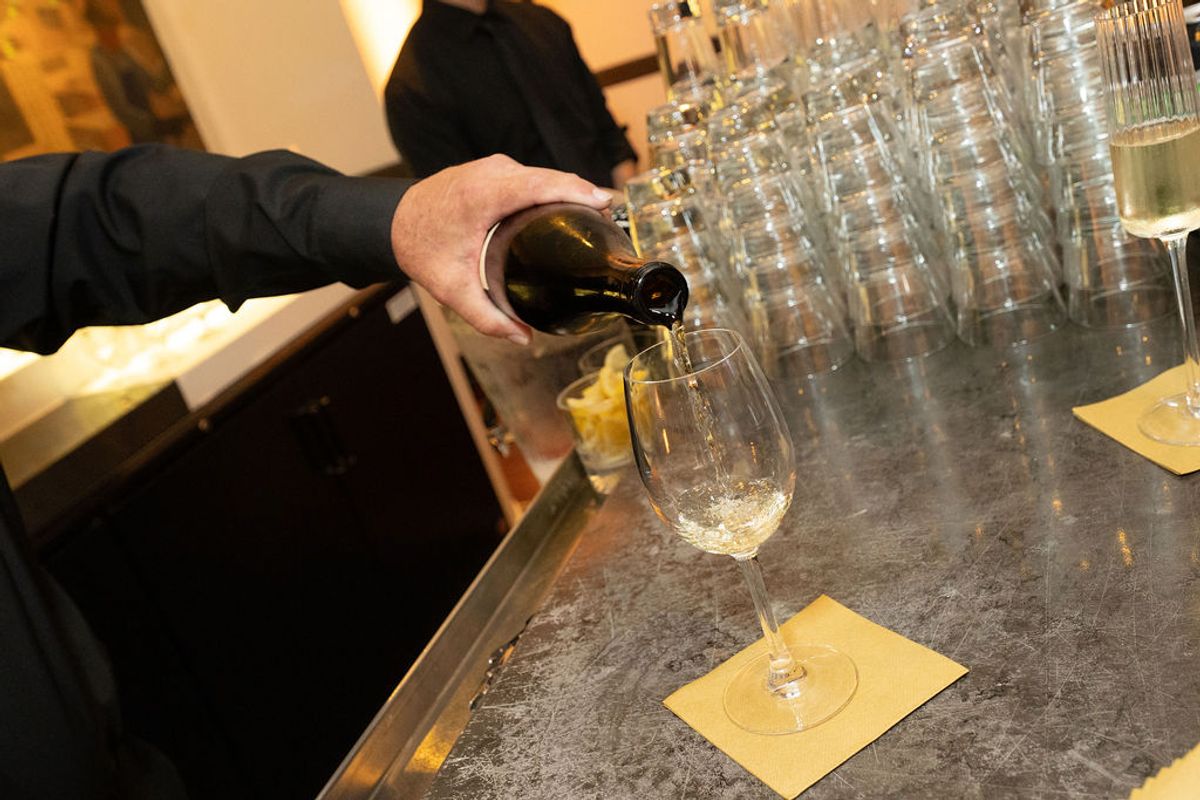 Person pouring wine into glass at networking reception with rows of wine glasses on dark counter