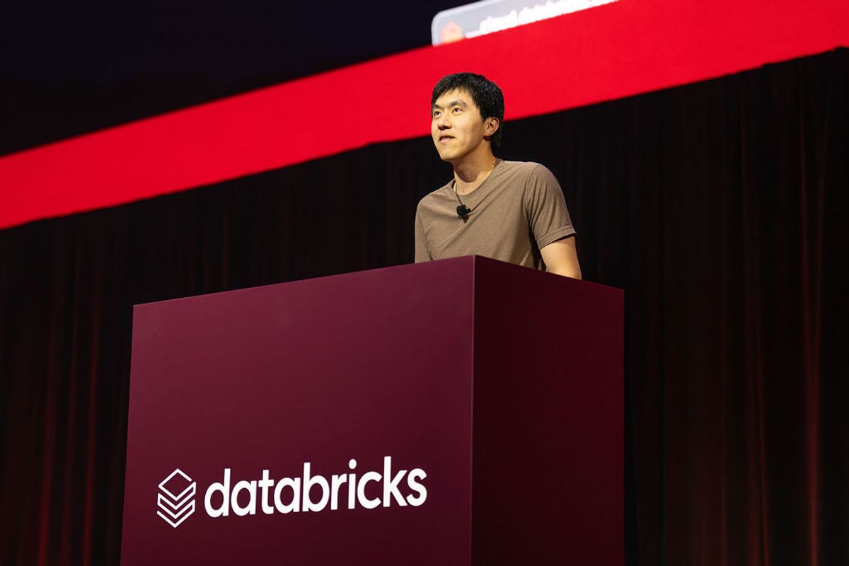 Speaker gesturing while presenting on stage with red branded backdrop at conference venue