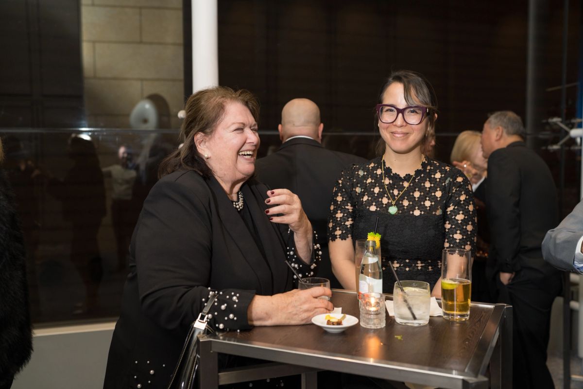 Two women networking at a cocktail table during an upscale evening event, smiling and conversing