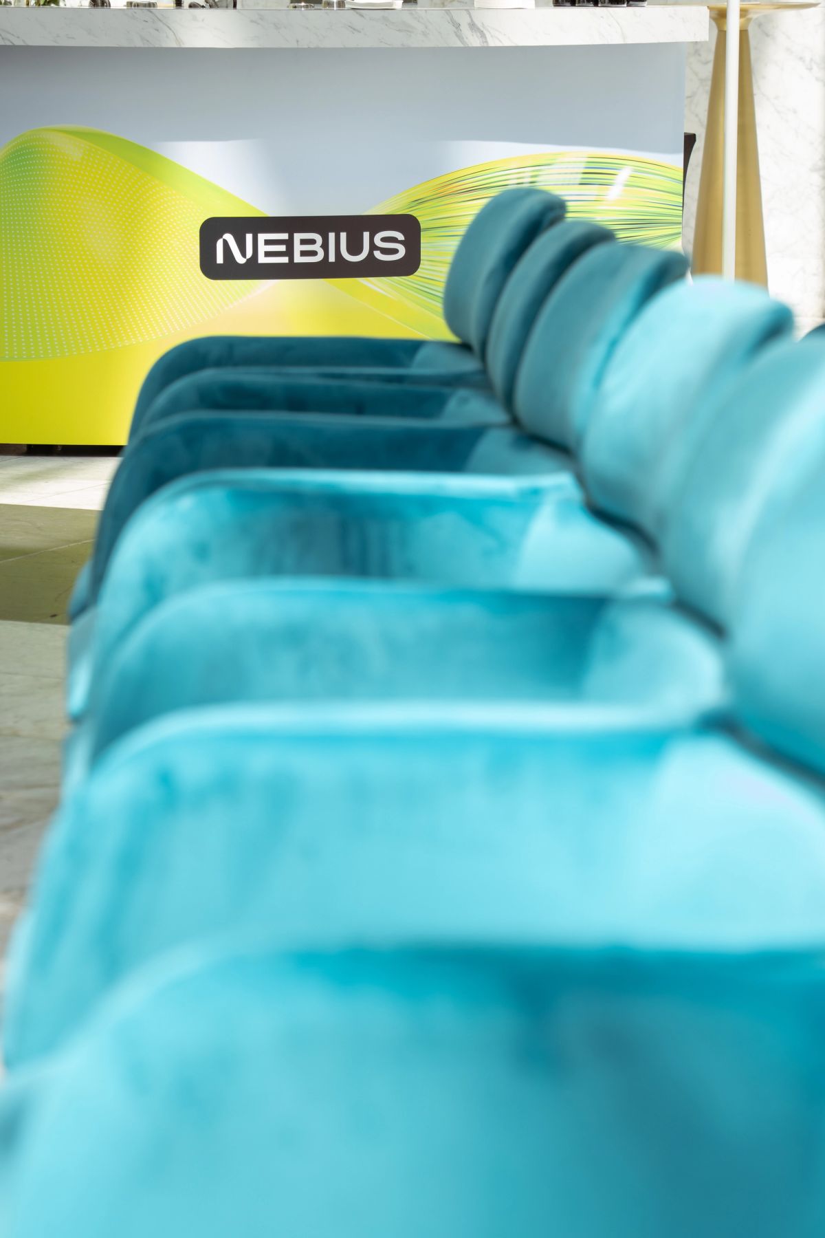 Teal lounge seating in foreground with Nebius branded backdrop at conference booth.